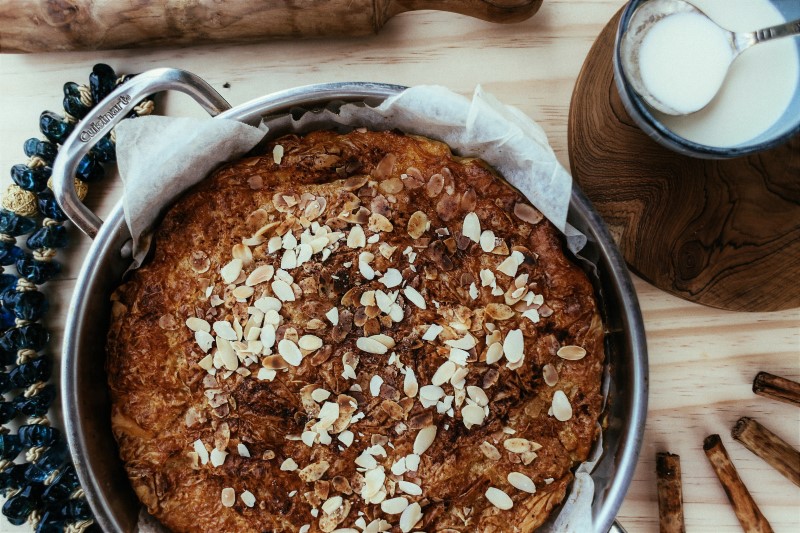Round almond cake in dish with assortment of ingredients and utensils scattered around